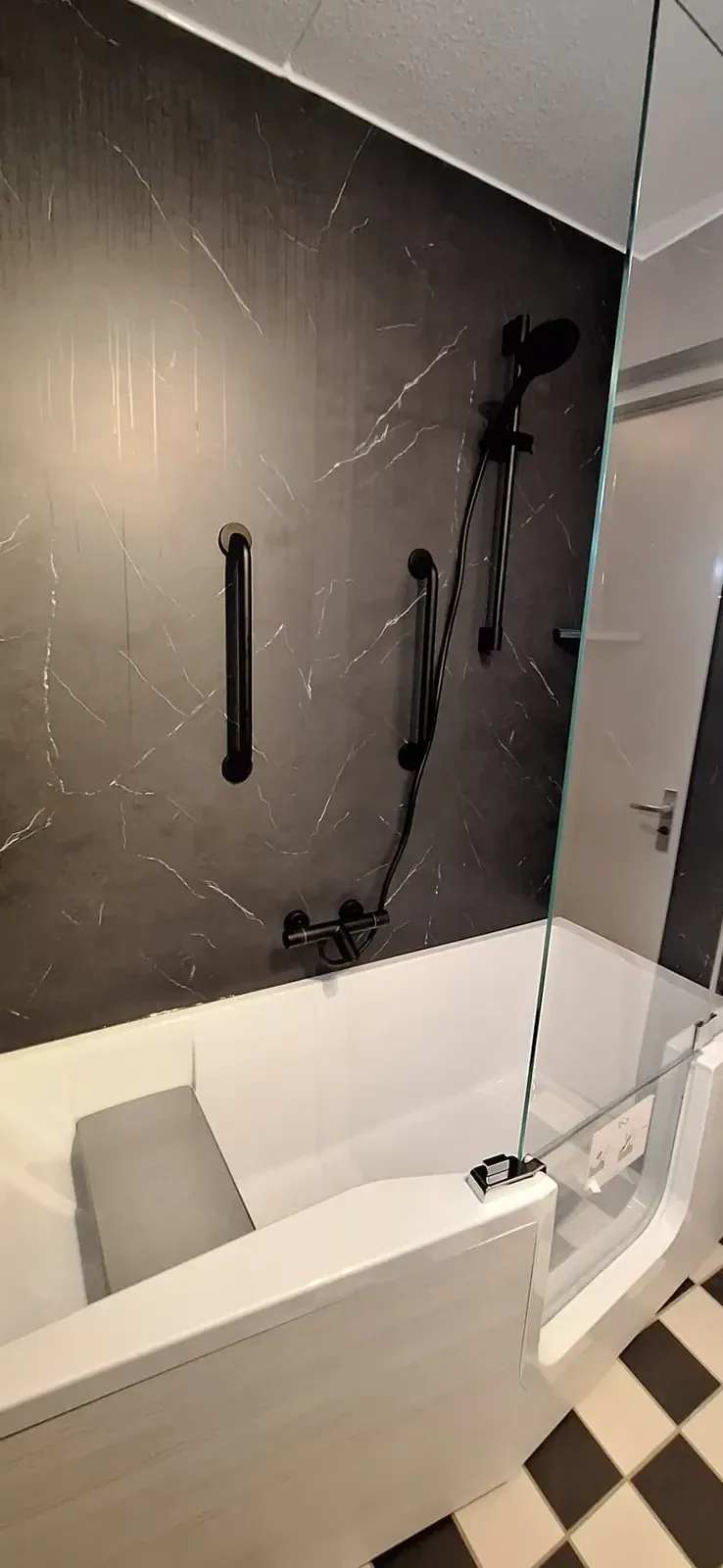 Bad met glazen badwand, zwarte marmerlook wandpanelen en zwarte steunbeugel en kranen