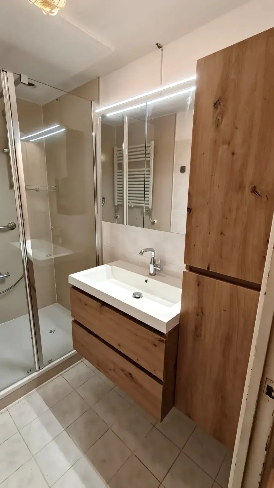 Badkamer met eiken wastafelmeubel, hoge kast, spiegelkast en douche met glazen deur