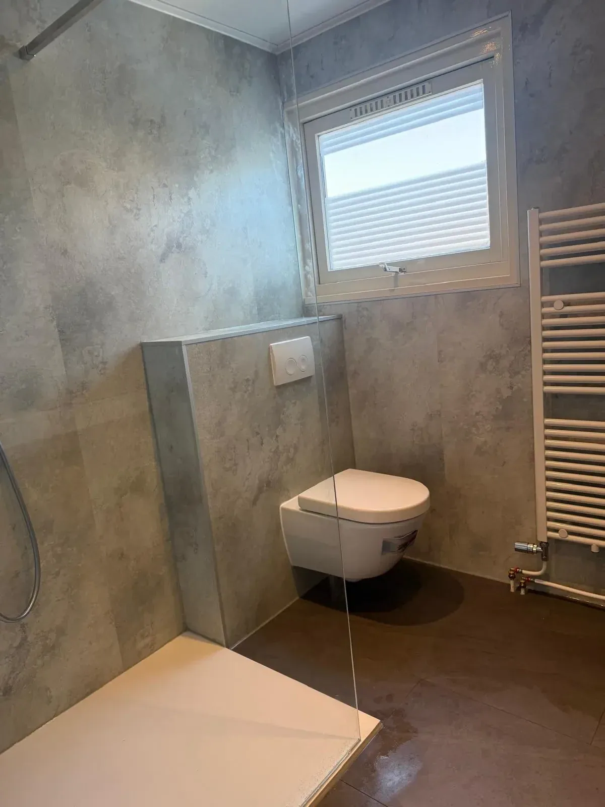 Badkamer met grijze wandpanelen, hangtoilet tegen voorzetwand, inloopdouche en handdoekradiator