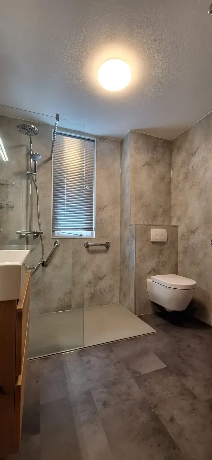 Badkamer met beige marmerlook wandpanelen, inloopdouche met regendouche en hangtoilet