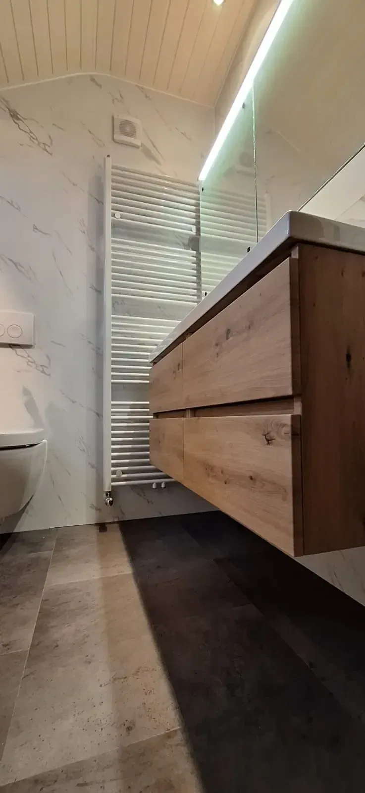 Badkamer met witte marmerlook wandpanelen, houtlook wastafelmeubel en witte handdoekradiator