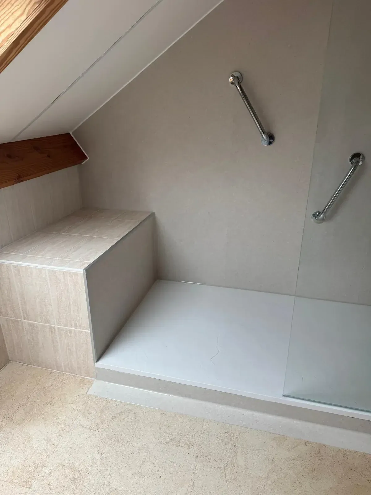 Douche met vaste zitbank, witte douchebak en twee steunbeugels op lichte wandpanelen onder schuin dak