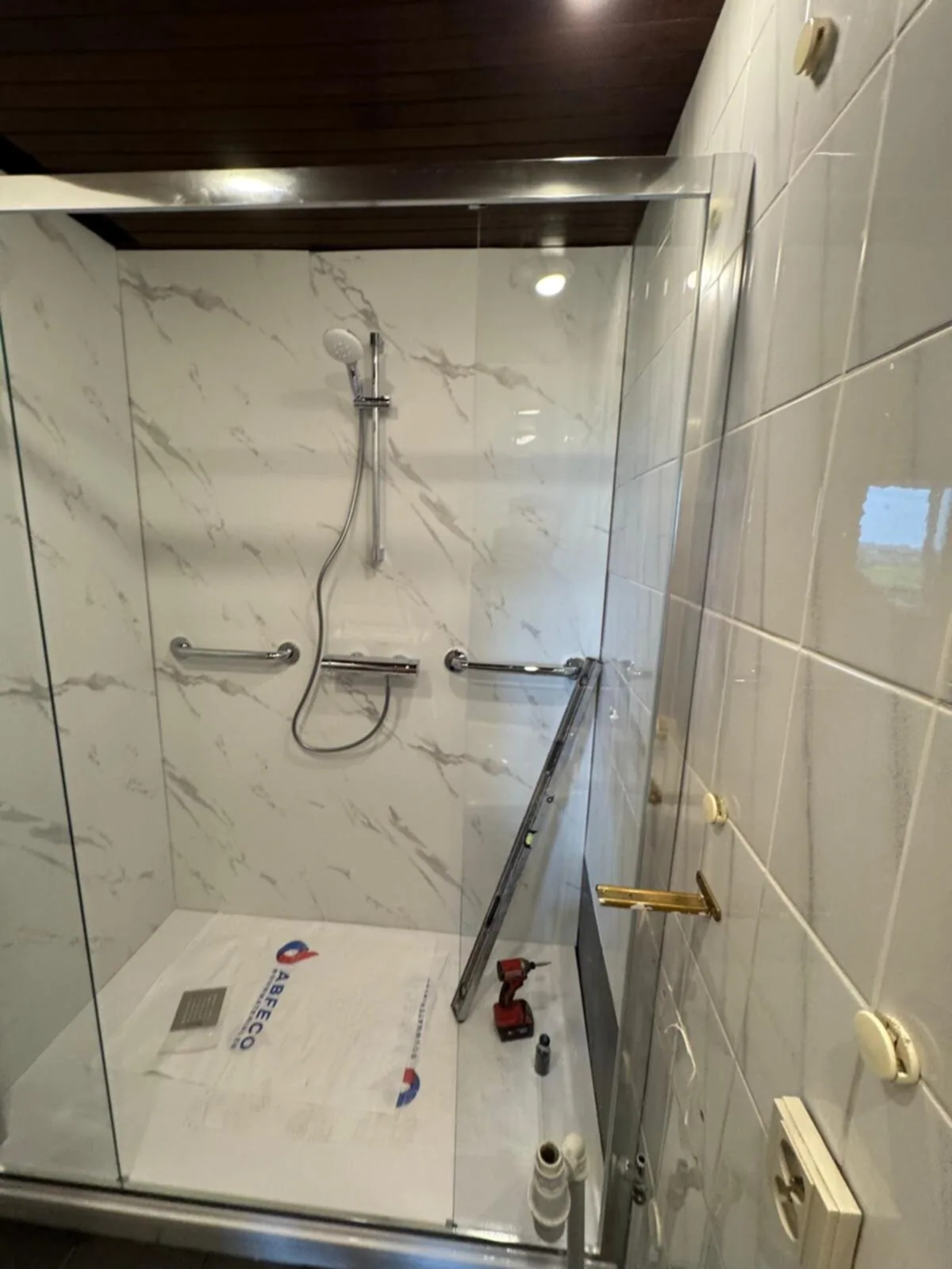 Douche tijdens afwerking: marmerlook panelen, thermostaatkraan, twee steunbeugels en een waterpas op de douchebak