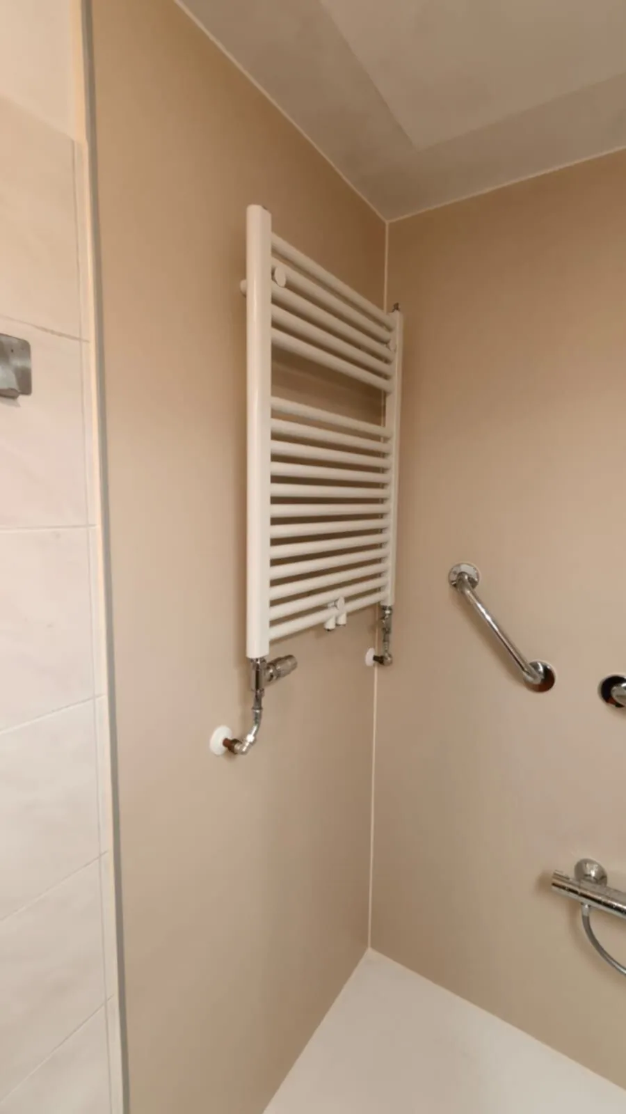 Douchehoek met beige wanden, witte handdoekradiator en steunbeugels