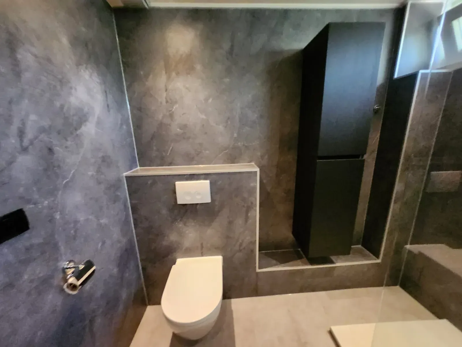 Wit hangtoilet op voorzetwand met donkergrijze marmerlook wandpanelen en hoge zwarte kast