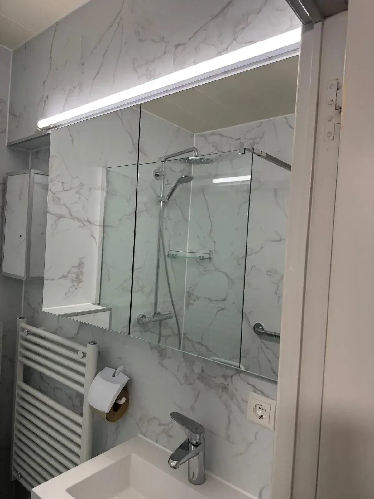 Kleine badkamer met marmerlook panelen, douche met glazen wand, radiator en wastafel