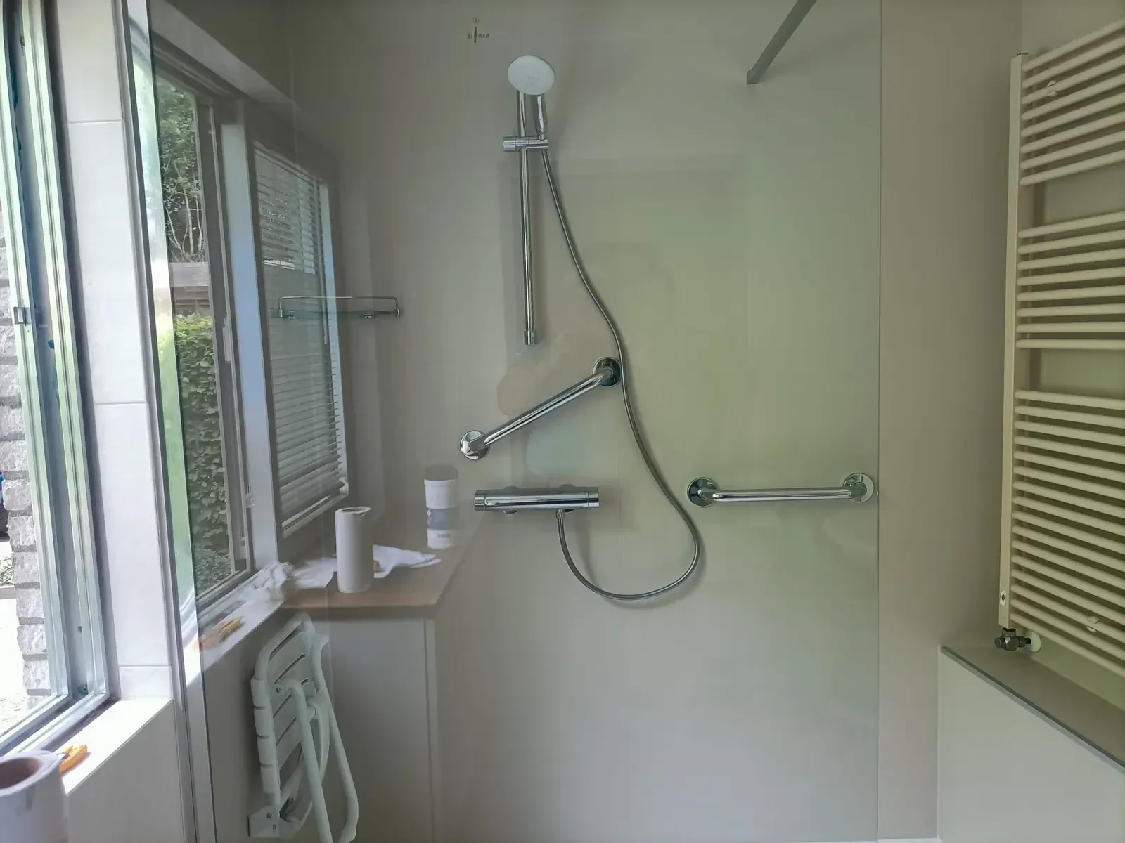 Lichte douche naast raam met thermostaatkraan, twee steunbeugels, opklapbaar zitje en witte radiator