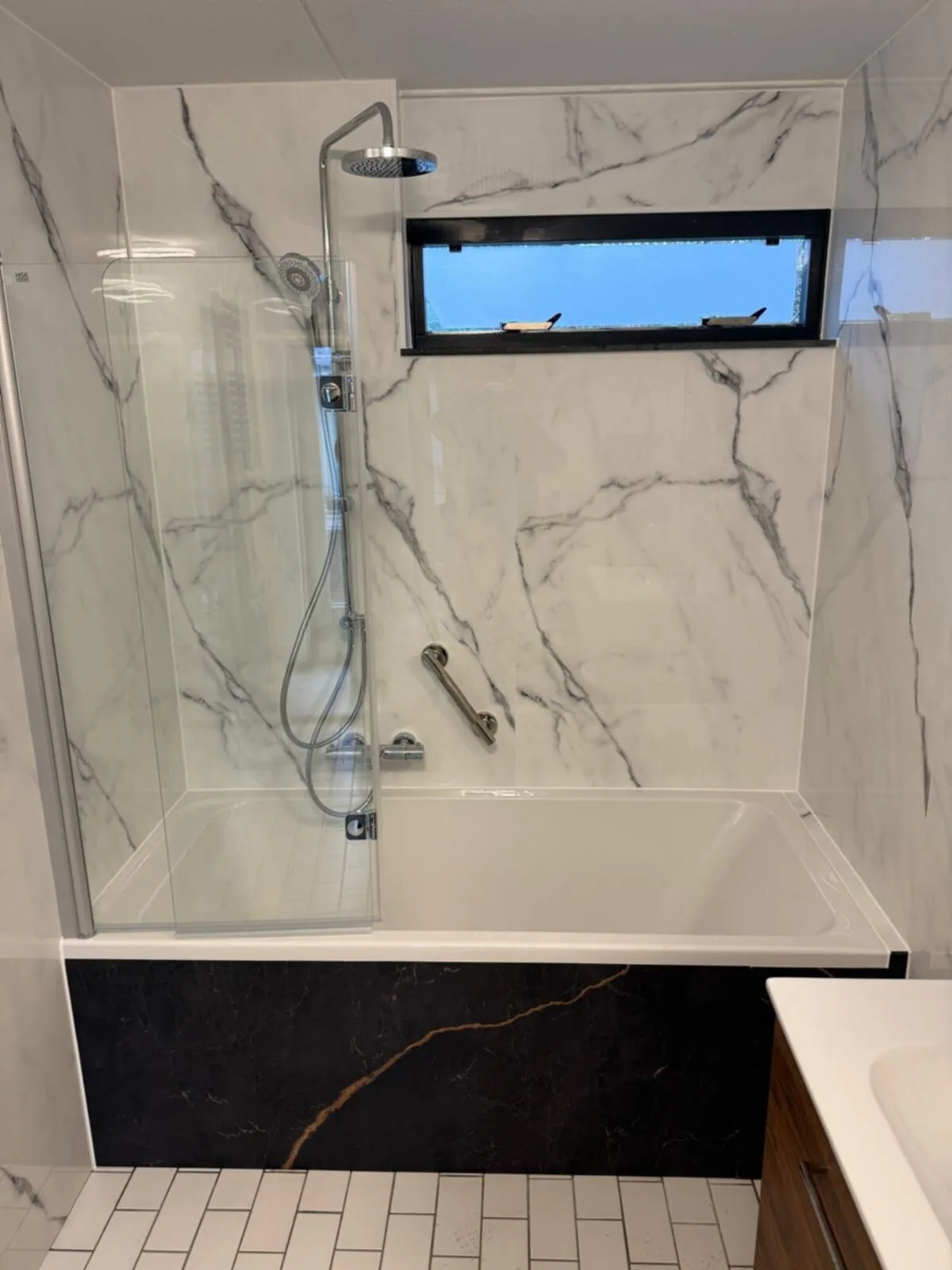 Ligbad met badwand, regendouche en steunbeugel tegen witte marmerlook wandpanelen