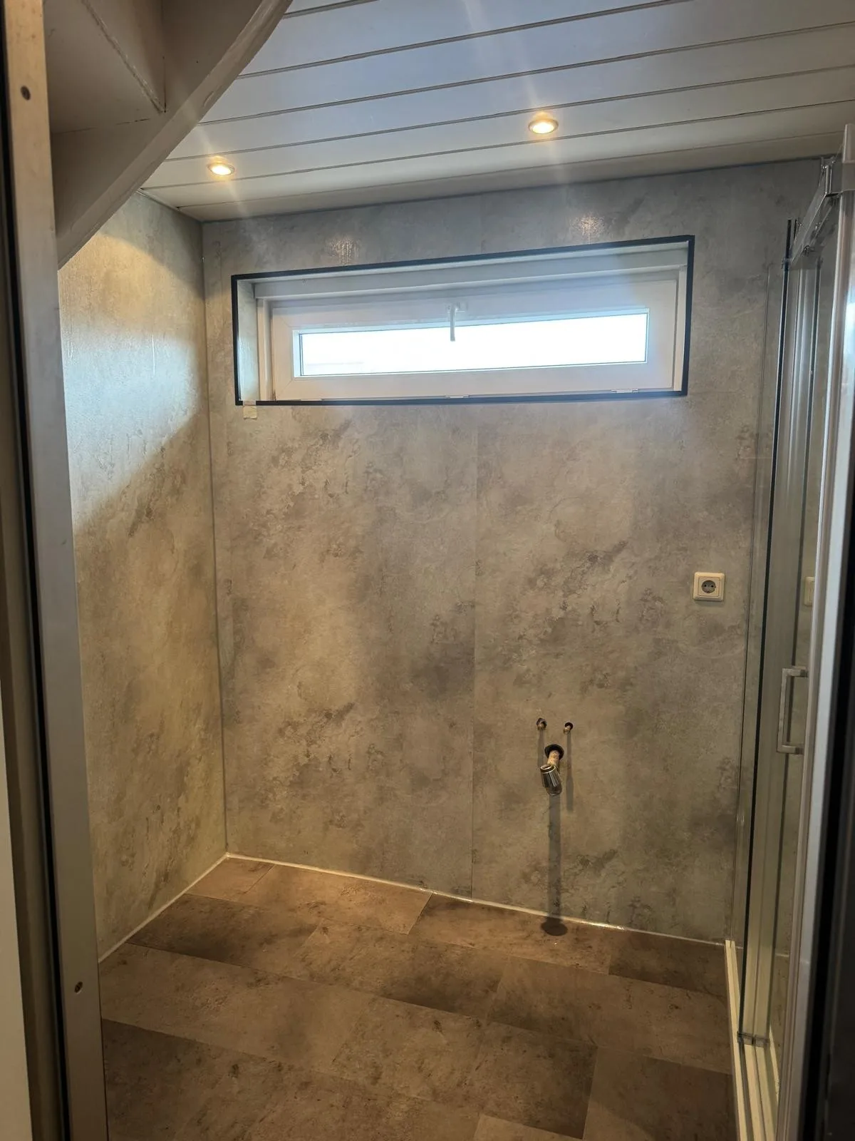 Lege ruimte met grijze marmerlook wandpanelen en klepraam, klaar voor de douche