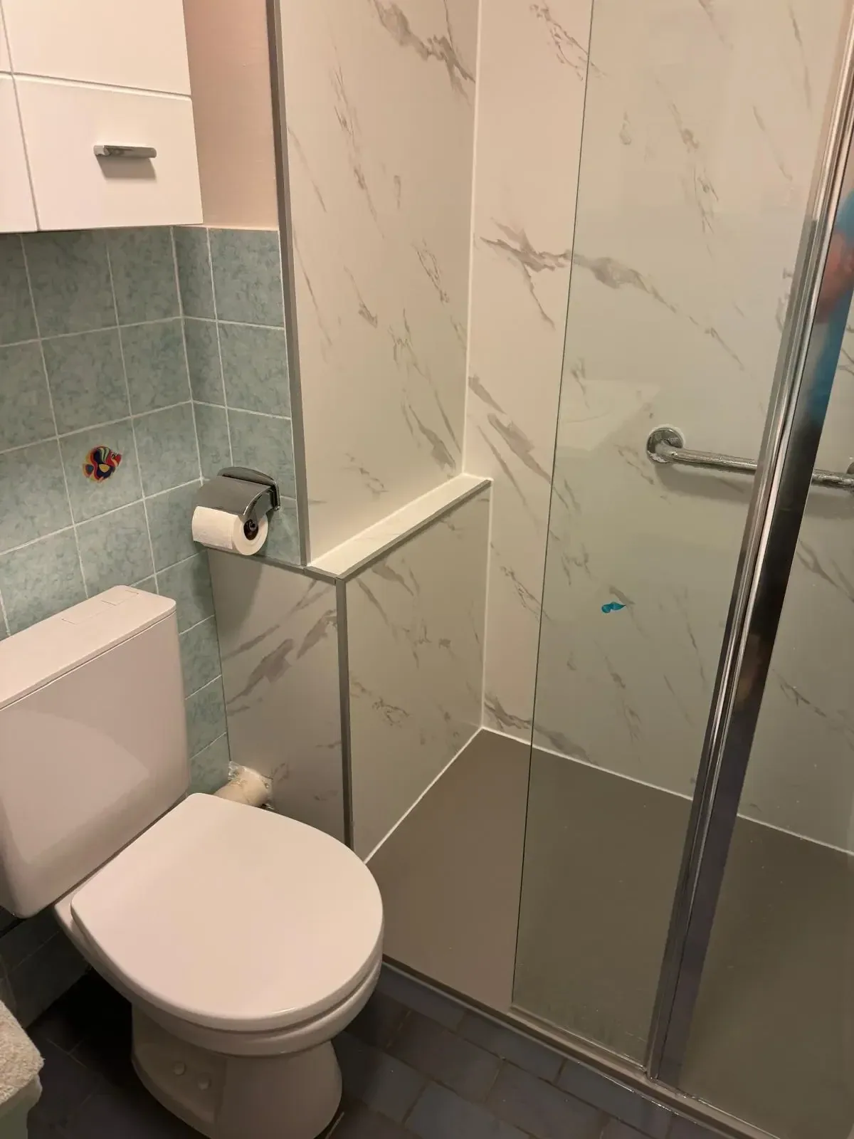 Staand toilet naast inloopdouche met witte marmerlook wandpanelen en steunbeugel