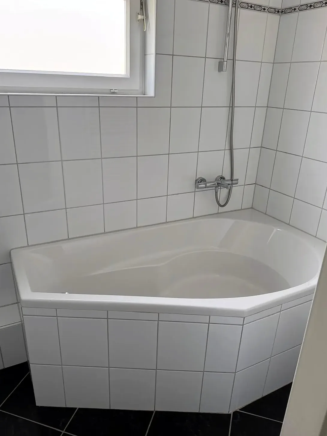 Voor: hoekbad met witte tegels onder het raam